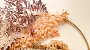 Getrocknete Pflanzen sind kreativ in einem goldenen Ring angeordnet.