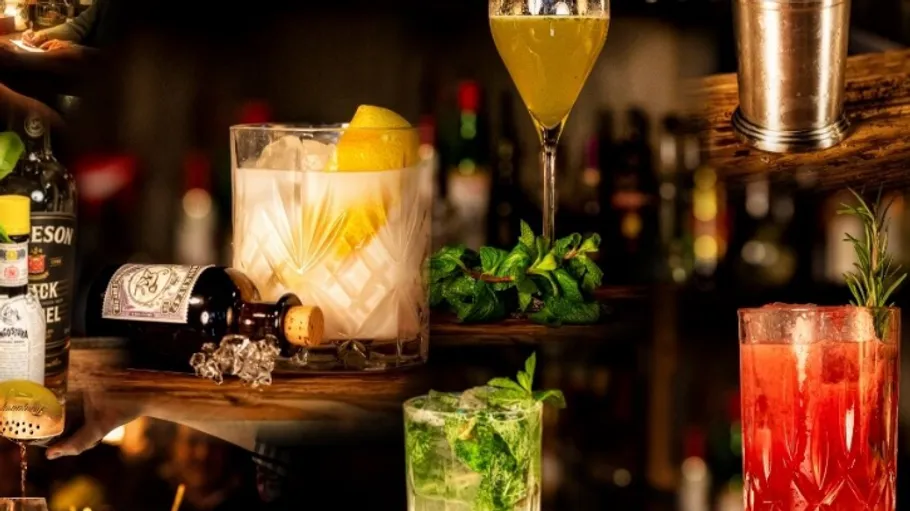 Cocktails sit on shelves surrounded by bottles and herbs.