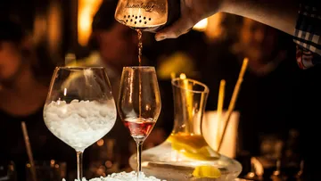 A bartender pours a cocktail into a glass.