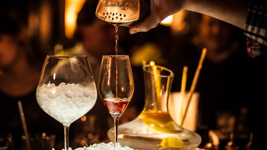 A bartender pours a cocktail into a glass.
