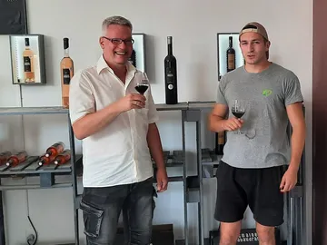 Two men hold wine glasses in a wine cellar.