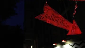 Red sign hangs: “Down the Rabbit Hole” at night