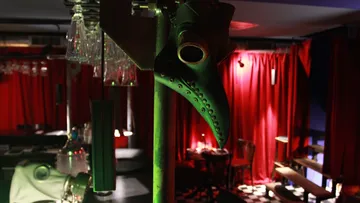 Ein Hahn mit einem Maskengesicht hängt über einer Bar.