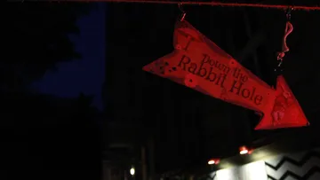 Rotes Schild weist den Weg zum Kaninchenbau bei Nacht.