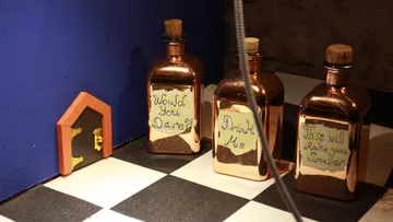 Drei Flaschen stehen neben einer kleinen Tür auf dem Boden.