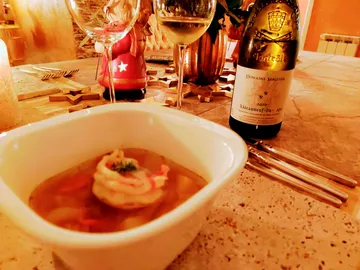 Schüssel mit Suppe, Weinflasche neben festlich gedecktem Tisch.