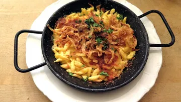 Pasta served with crispy onions in a black plate.