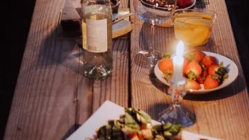 Table with food and drinks, lit by candlelight.