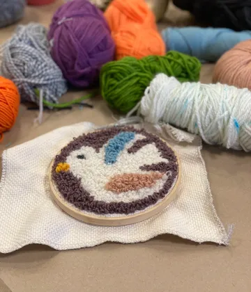 An embroidered bird image in an embroidery frame lies on fabric.