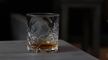 A glass of whiskey is on a table.
