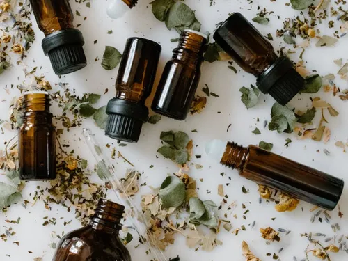 Brown vials lie on a white surface with herbs.