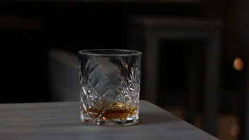 Ein Glas mit dunkler Flüssigkeit steht auf einem Tisch.