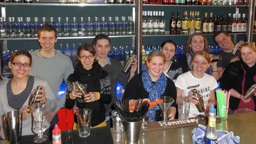 Mehrere Menschen mixen Cocktails hinter einer Bar.