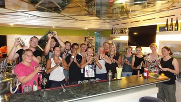 Gruppe von Menschen schüttelt Cocktailshaker an der Bar.