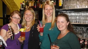 Vier Frauen halten Cocktails in einer Bar und lächeln.