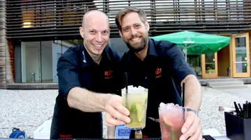 Zwei Barkeeper präsentieren frische Cocktails an der Bar.