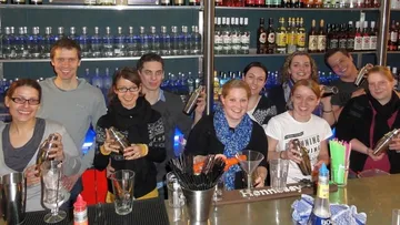 Gruppe von Menschen schüttelt Cocktails hinter einer Bar.