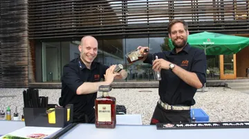 Zwei Barkeeper mixen Cocktails an einer Bar im Freien.