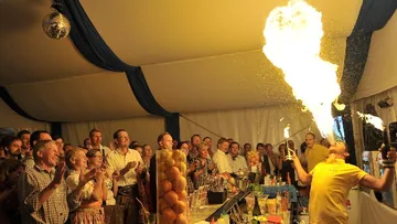Bartender breathes fire, audience applauds in tent.