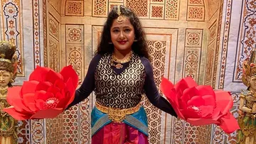Woman holding red paper flowers against an ornamental background.