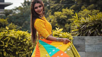 Woman in colorful dress dances in front of green plants.