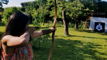 A person aims a bow at an outdoor target.
