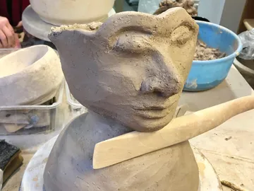 Tonfigur mit Gesichtszügen, wird mit Werkzeug bearbeitet.