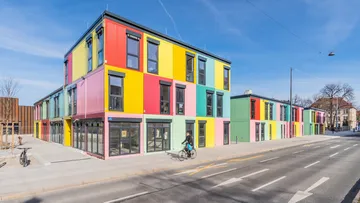 Colourful building stands on a street, cyclists pass by.