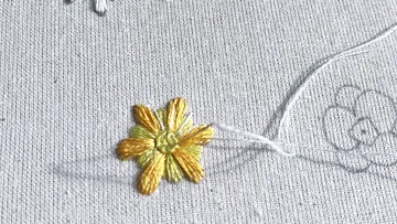 Gestickte Blume auf hellem Stoff, Faden sichtbar.