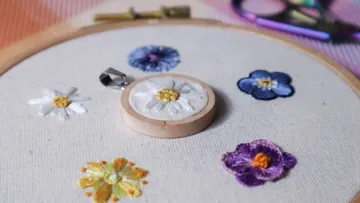 Gestickte Blumen in einem Rahmen, eine Blume im Mittelpunkt.