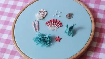 Gestickte Muscheln und Meereslebewesen auf blauem Stoff.