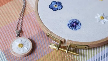 Embroidered flowers on a fabric frame next to a necklace with a pendant