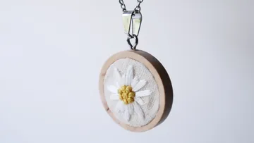 Necklace with round flower hanging in a wooden frame.