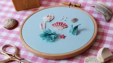 Gestickte Muscheln und Sterne auf blauem Stoff, umgeben von Dekor.