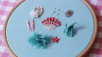 Embroidered shells and marine life on blue fabric.