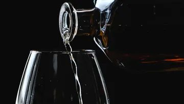 A bottle pours liquid into a glass against a black background.