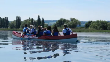 Gruppe im Kanu rudert über ruhiges Wasser, umgeben von Bäumen.