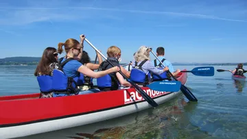 Menschen paddeln in einem Kanu auf ruhigem Wasser.