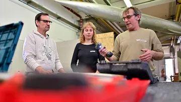 Three people stand around a table and discuss tools.