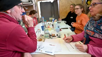 Gruppendiskussion am Tisch, Teilnehmer interagieren mit Materialien.