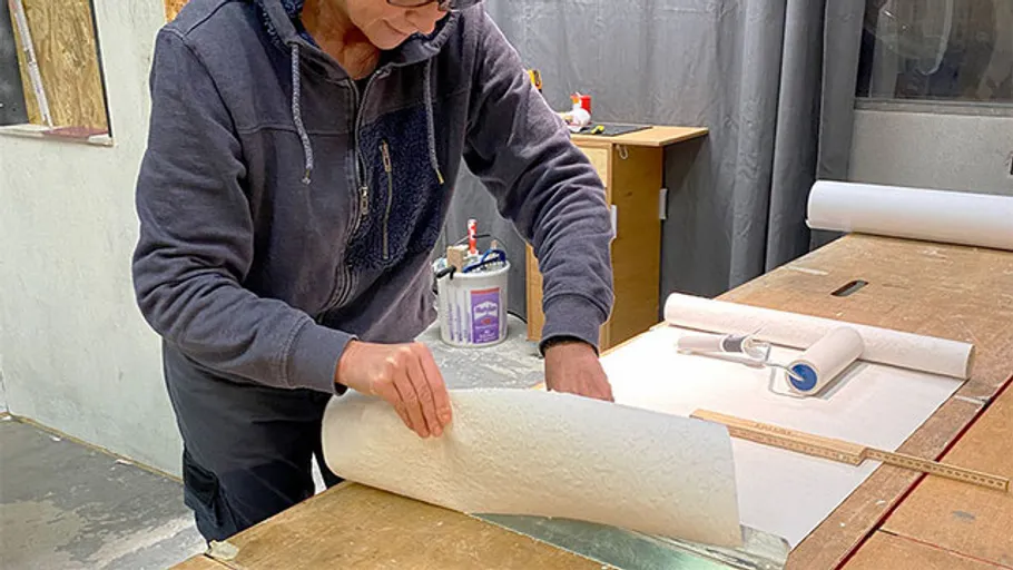 Person rollt Tapete auf einem Tisch in einem Arbeitsraum.