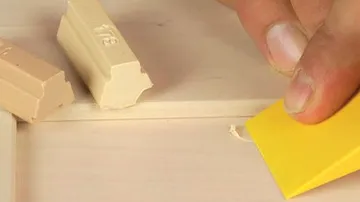 Eine Hand benutzt einen gelben Schaber auf Holzoberfläche.