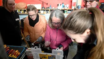 Fünf Personen untersuchen Werkzeug in einem Arbeitsraum.