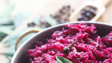 Rote Kohl in einem Topf, umgeben von Gewürzen und Blättern.