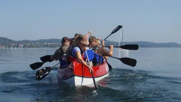 Ruderboot fährt auf ruhigem Wasser, besetzt mit Menschen.