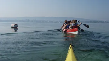 Kajakfahrer rudern auf ruhigem Wasser, umgeben von Bergen.