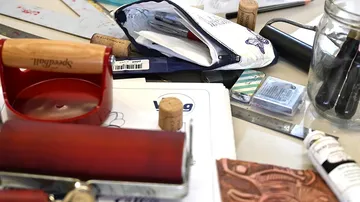 Red paint roller is lying on a table with art materials.