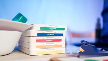 Bunte Farbkästen stehen auf einem Tisch neben Geschirr.