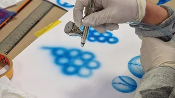 Luftdruckpistole sprüht blaue Farben auf ein Papier.