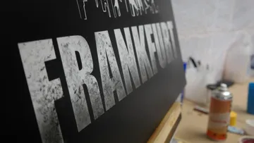 Schwarze Tafel mit dem Wort `FRANKFURT` im Vordergrund.